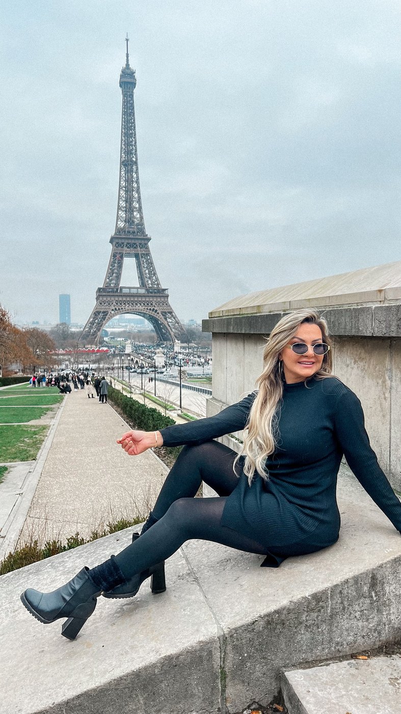 Dani em Paris, sentada com a Torre Eiffel ao fundo