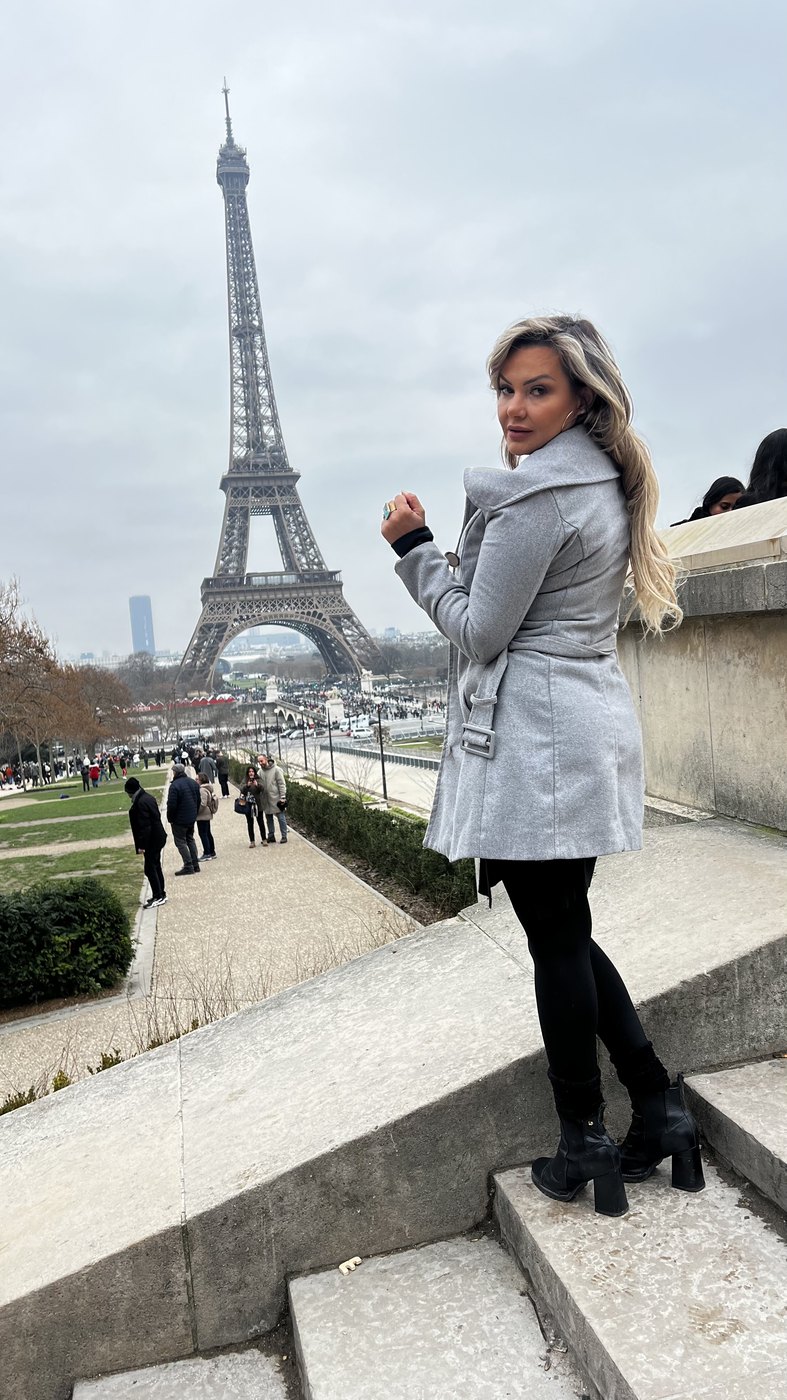 Dani em Paris, de casaco cinza, na frente da Torre Eiffel